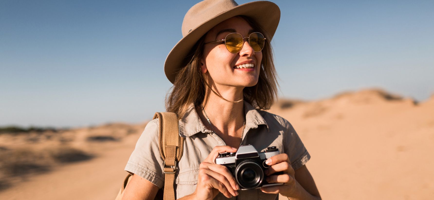 Mujer en el desierto, posa feliz con un sombre y una cámara fotográfica
